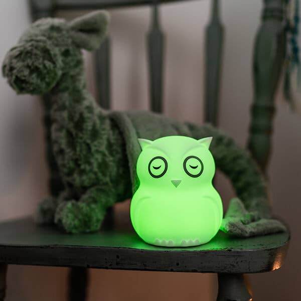 Green owl-shaped night light on a table with a plush toy in the background