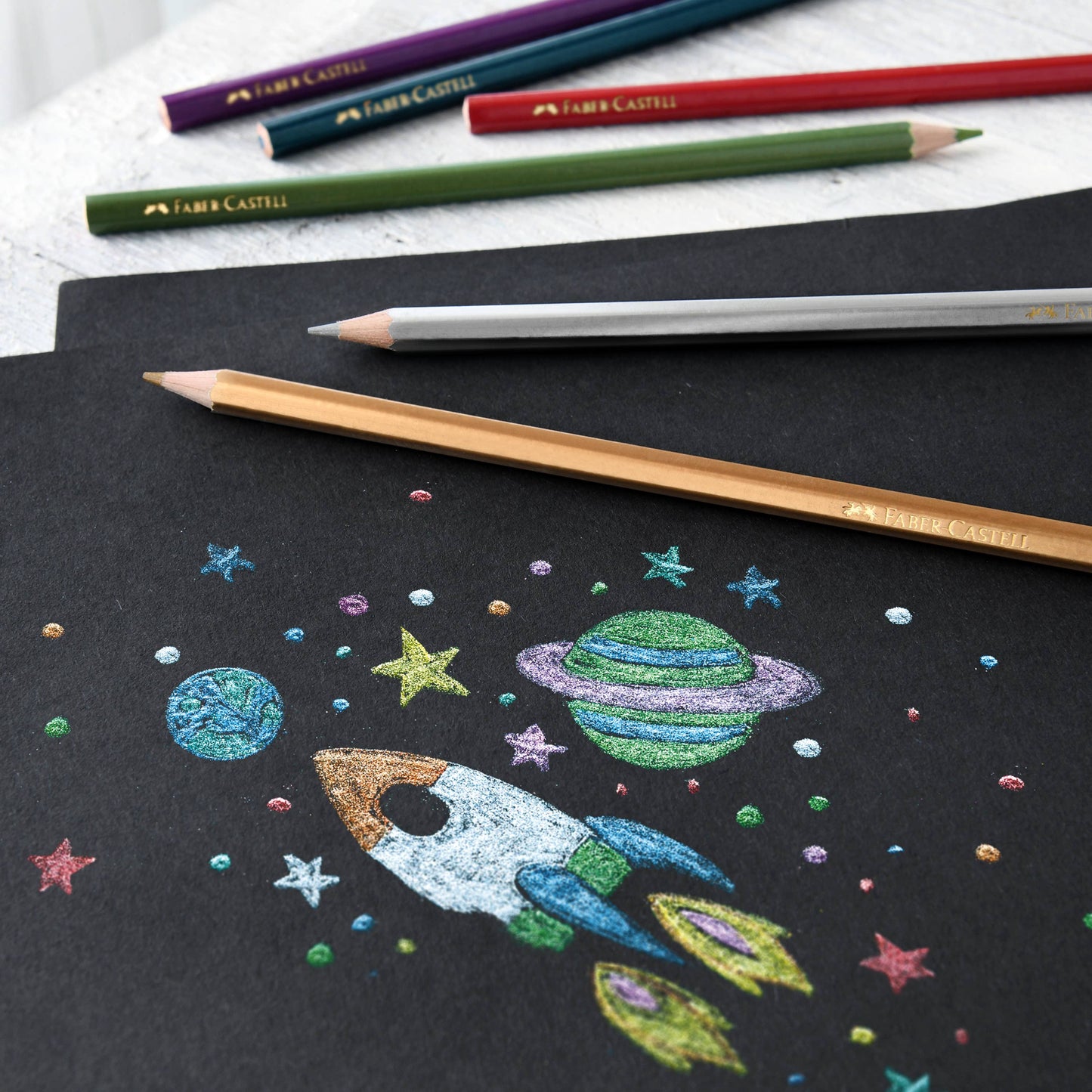 Colorful space-themed drawing on black paper with colored pencils.