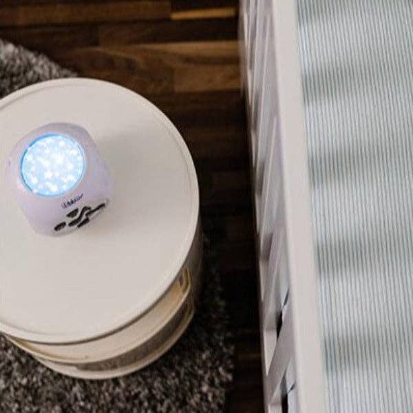 Small round device with a blue light on top of a stack of books next to a radiator.