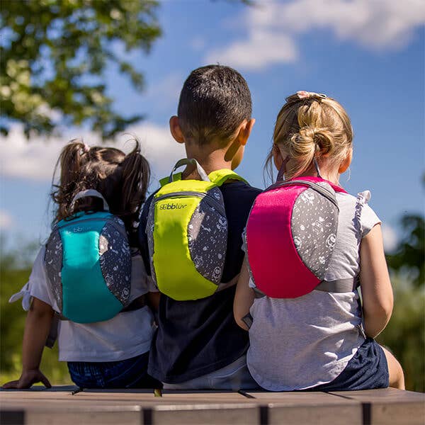 Three children with colorful backpacks sitting on a bench outdoors.