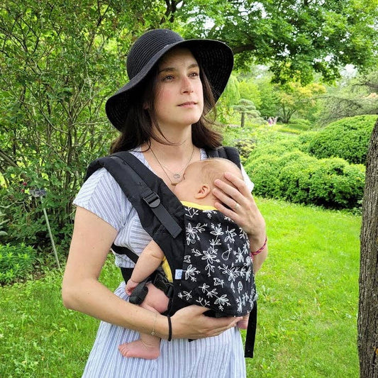 Woman holding a baby in a sling outdoors in a park