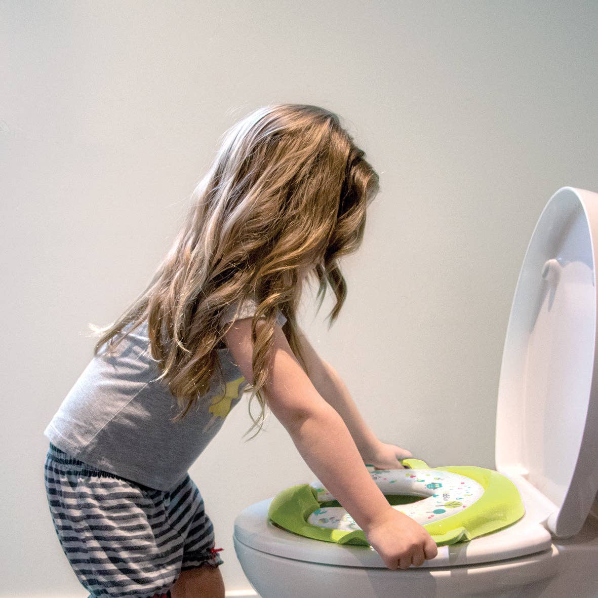 Child using a green potty seat on a toilet with a plain background