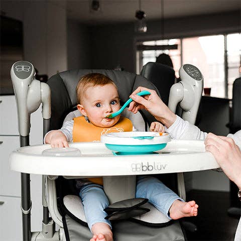Baby in a high chair being fed by an adult, with a focus on the high chair brand 'Bbluv'.