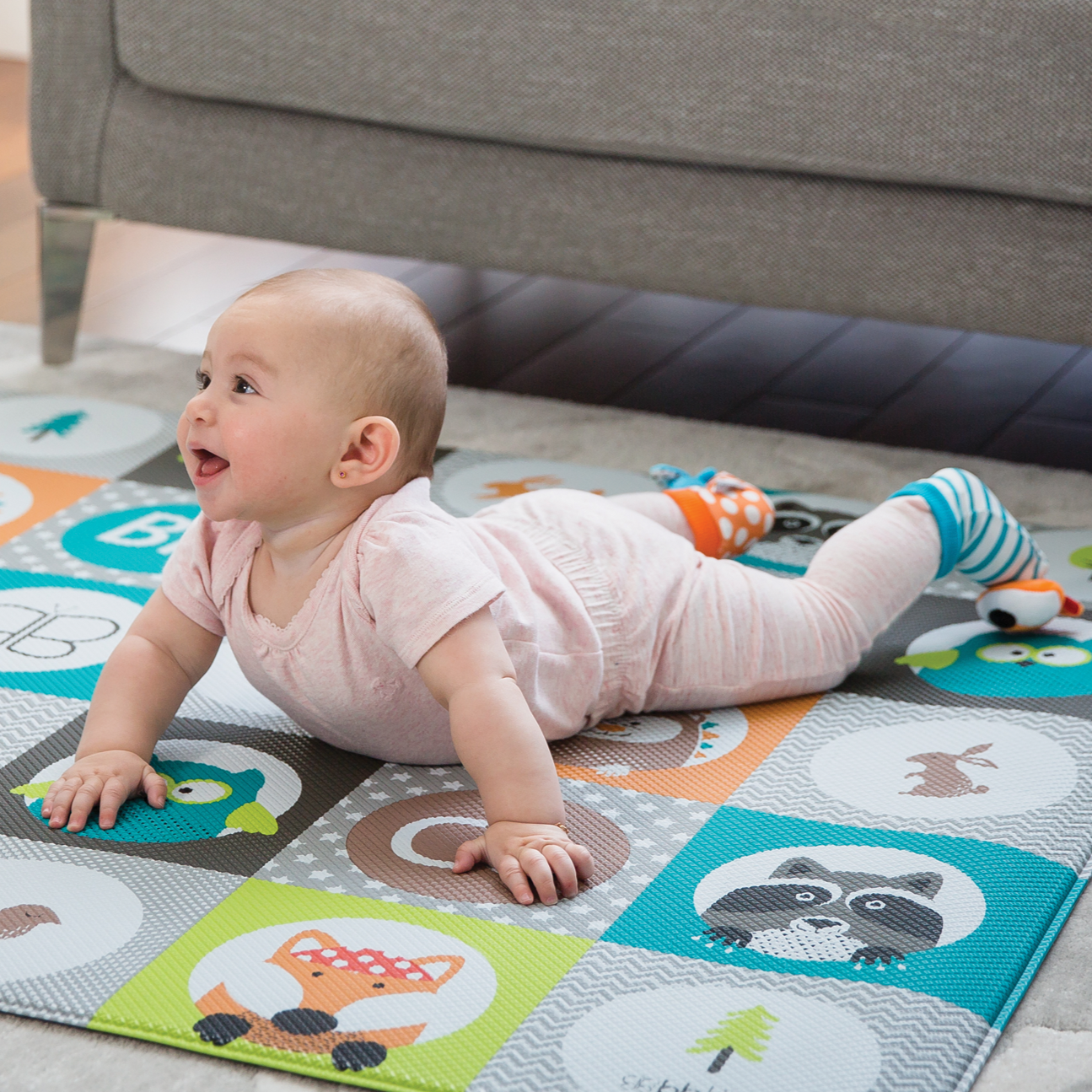 Baby playing on a colorful play mat with animal designs in a living room.
