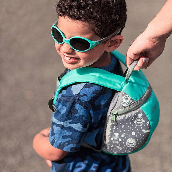 Child wearing sunglasses and a backpack with a gray interior, standing on a concrete surface.