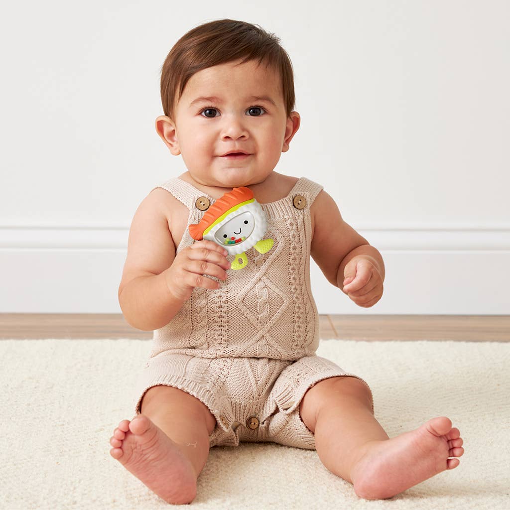 Baby sitting on a white surface holding a colorful teether