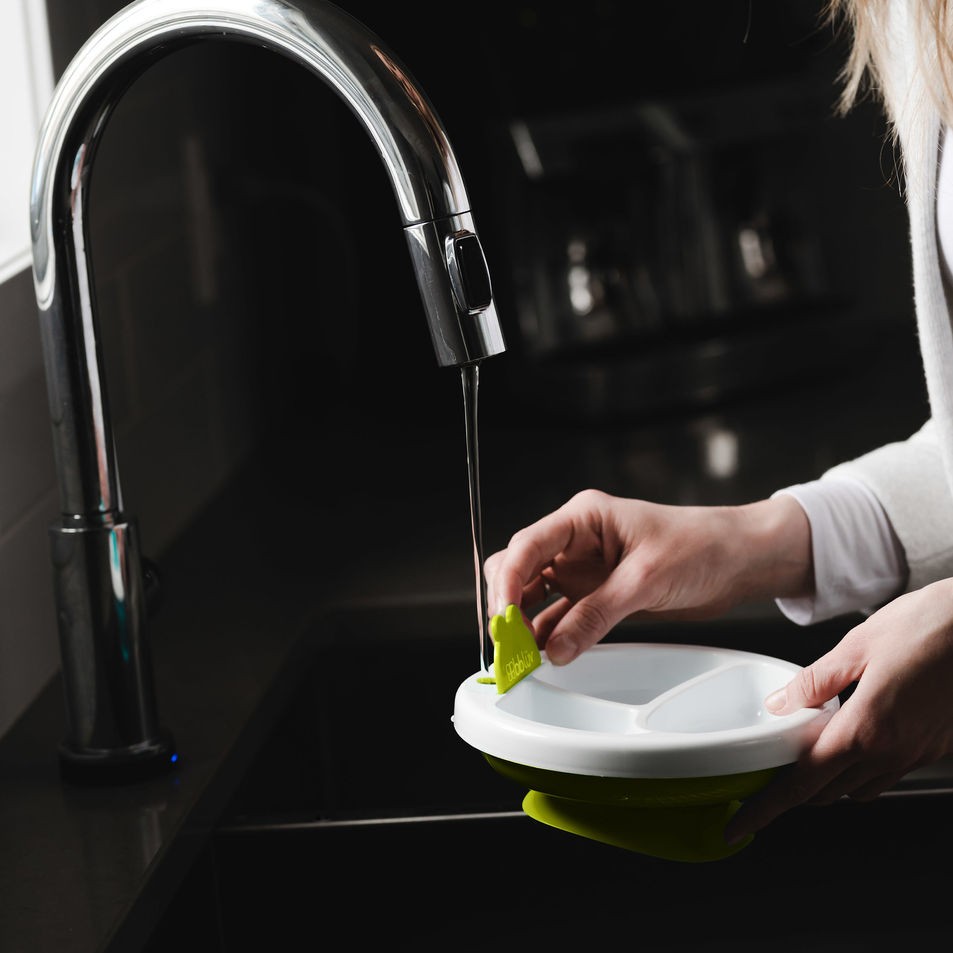 Person washing a green and white plate under running water from a kitchen faucet.