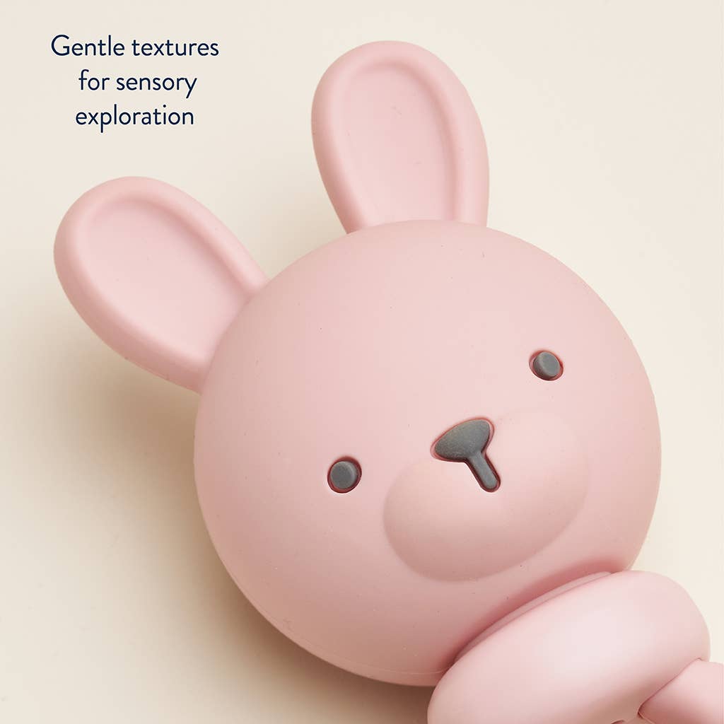 Pink bunny rattle with text 'Gentle textures for sensory exploration' on a beige background