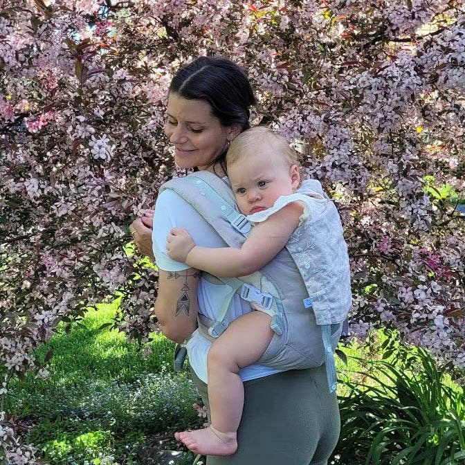 Woman holding a baby in a carrier with cherry blossom trees in the background