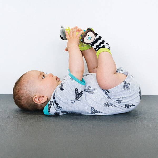 Baby lying on a gray surface holding a sock with a white background