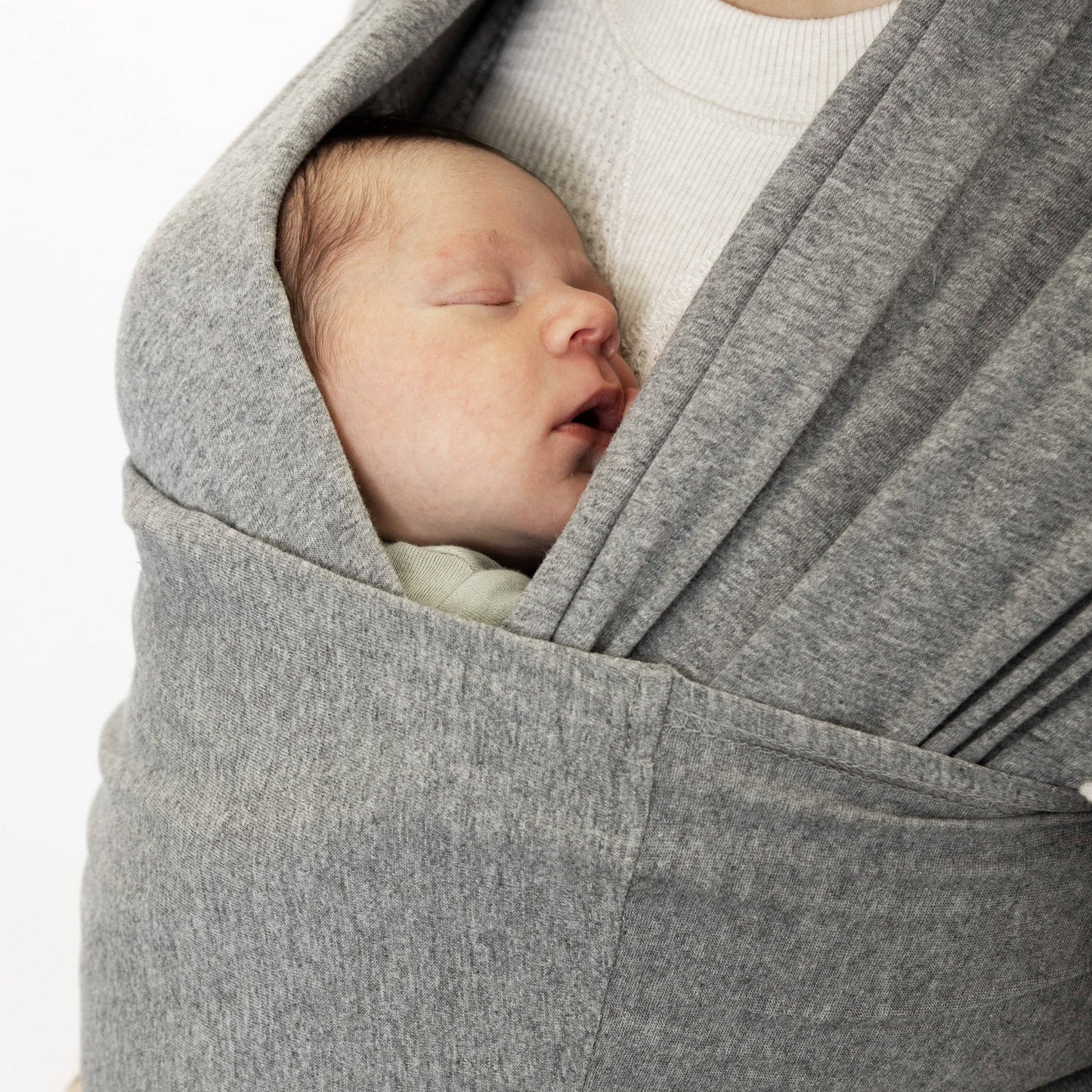 Newborn baby sleeping in a gray baby wrap carrier.