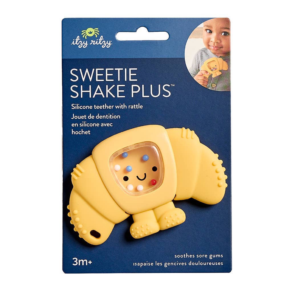 Yellow croissant-shaped silicone teether with rattle in packaging on a white background