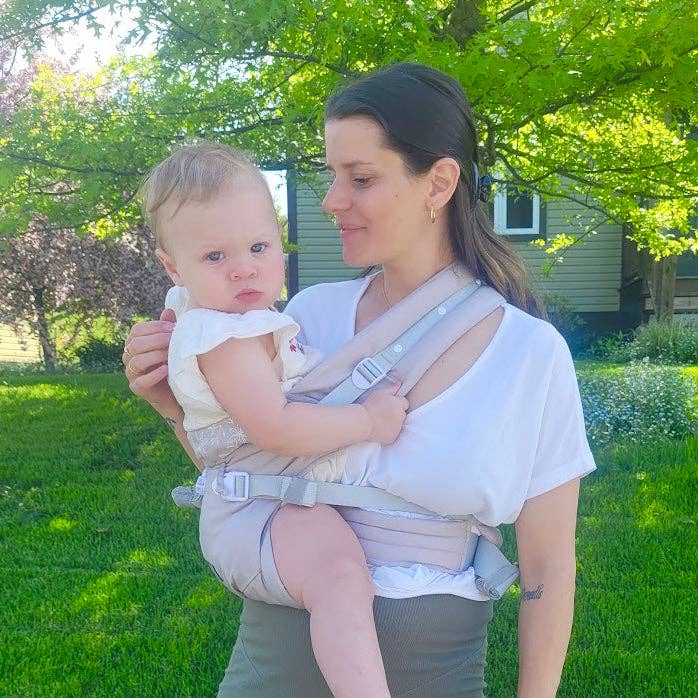 Woman holding a baby in a carrier outdoors on a sunny day