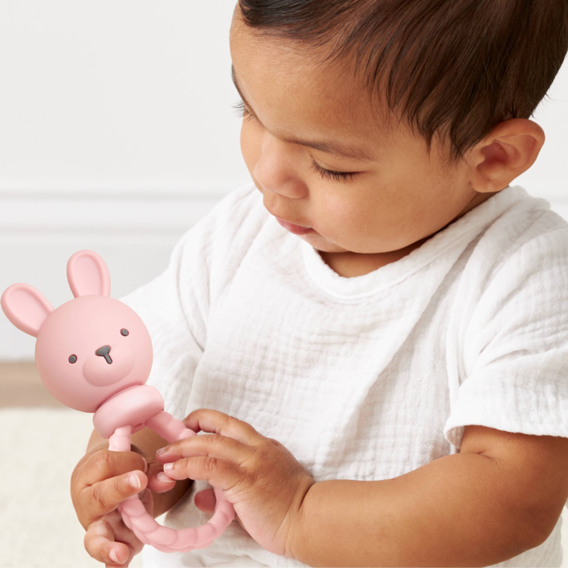 Baby holding a pink bunny-shaped rattle against a white background