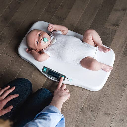 Baby lying on a digital scale with a person using the scale's controls.