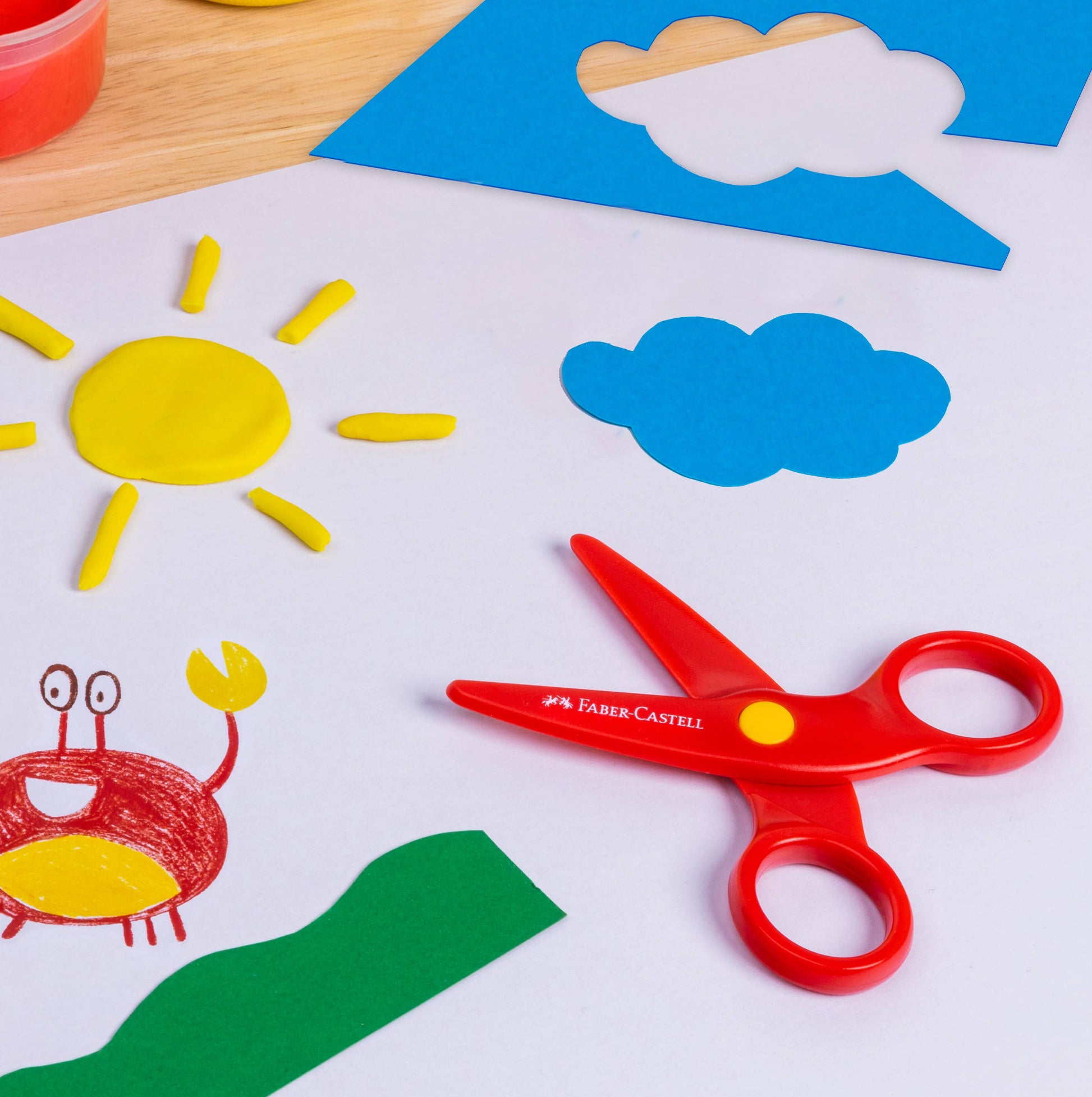 Children's craft materials including scissors, paper cutouts of a sun, cloud, and crab on a white surface.