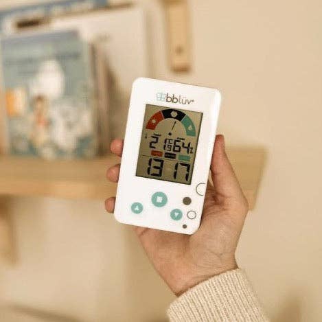 Hand holding a digital thermometer with a blurred indoor background