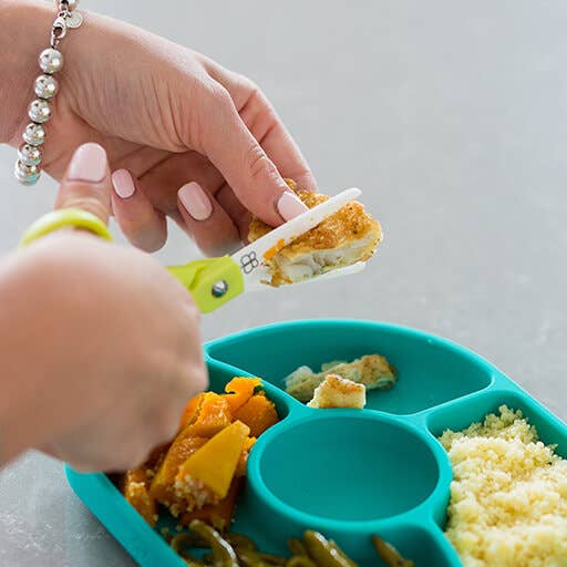 Person using a green and yellow spoon to feed food from a teal divided plate.
