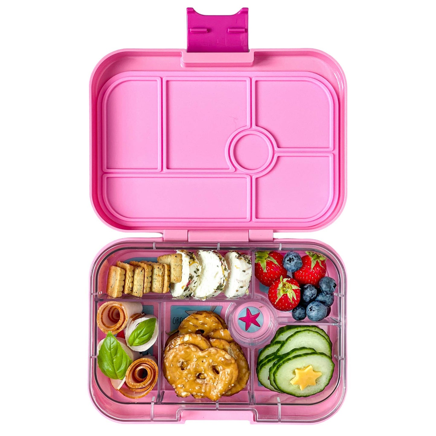 Pink Yumbox lunch box filled with food on a white background