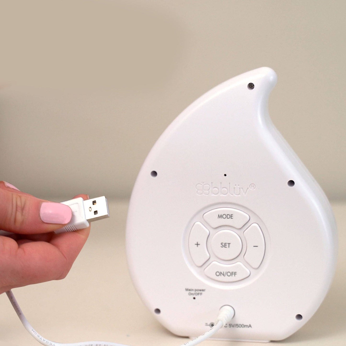 White electronic device with USB connection held by a hand against a beige background