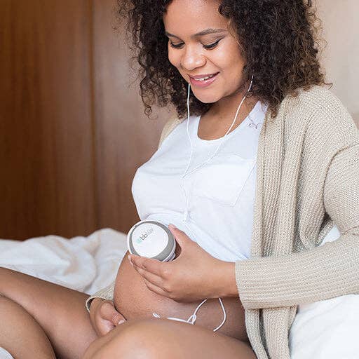 Woman holding a heart rate monitor with earphones, sitting on a bed.