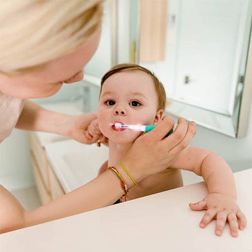 Woman teaching a baby how to use a toothbrush in a bathroom setting