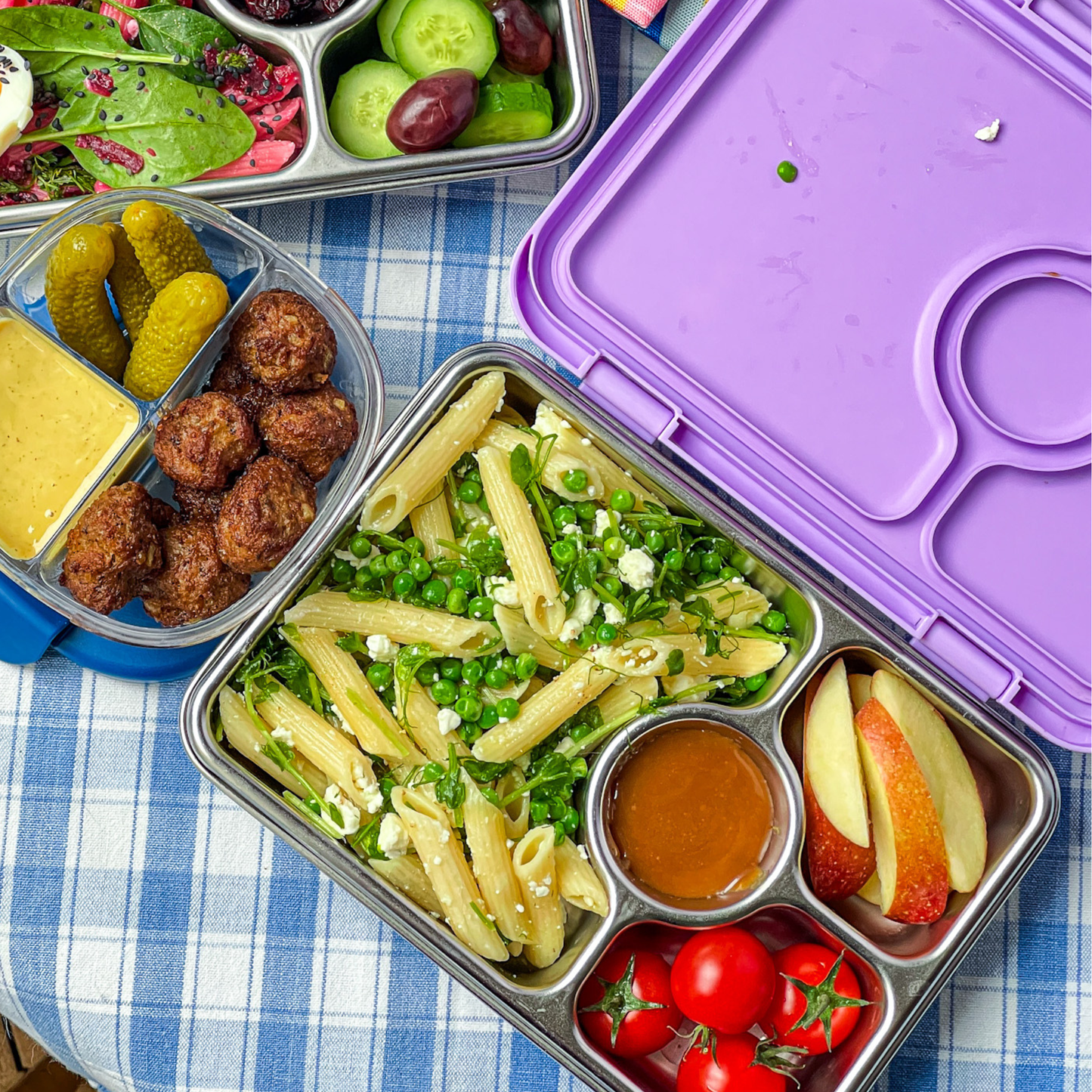 Yumbox with purple lid, full of food, placed on a blue and white gingham tablecloth