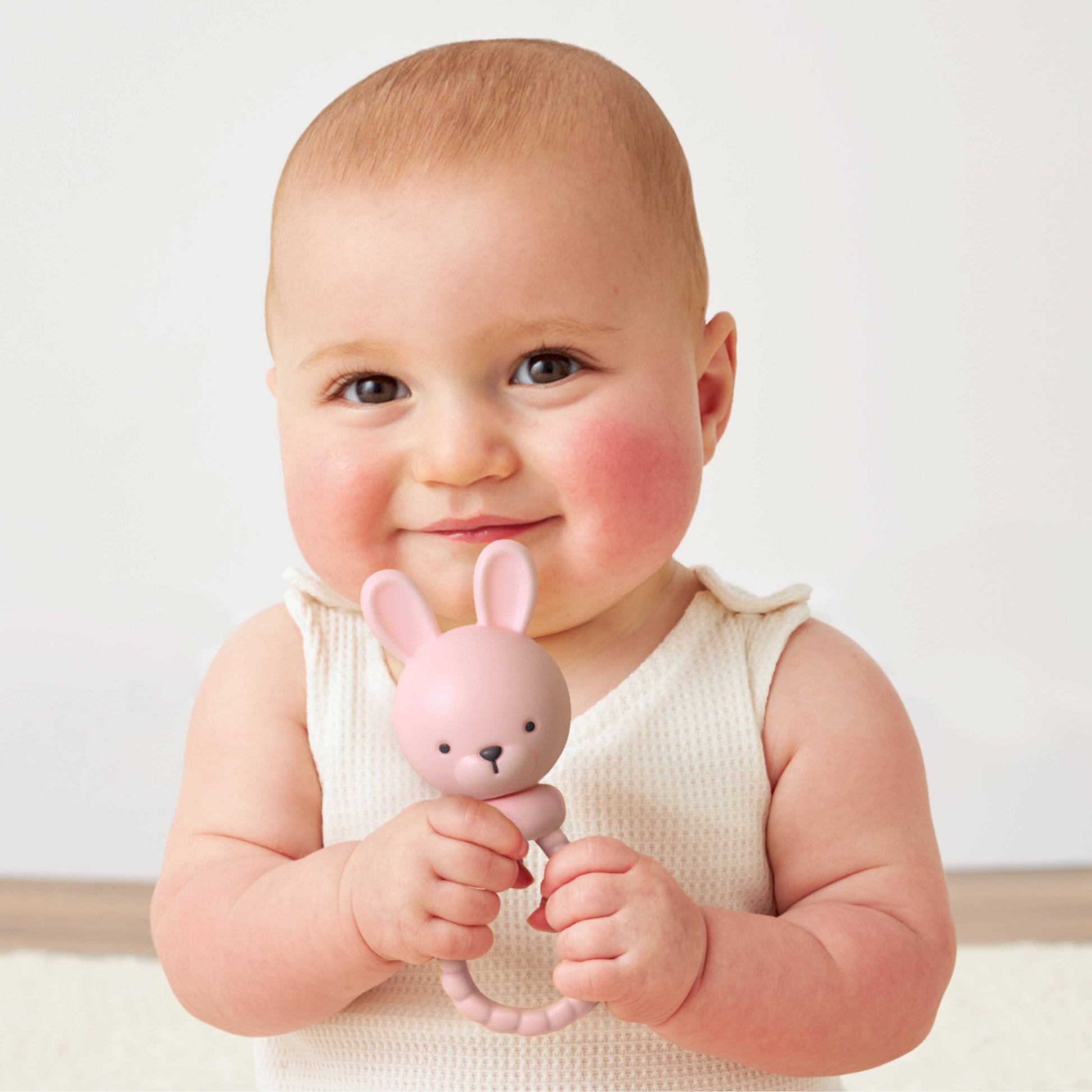 Baby holding a pink bunny toy against a white background
