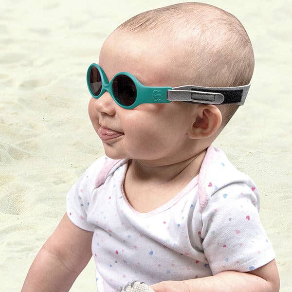 Baby wearing teal sunglasses on a sandy background