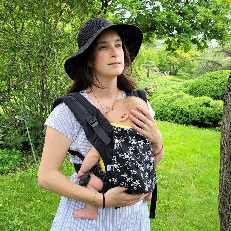 Woman holding a baby in a sling outdoors in a park